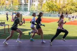 Cztery biegaczki w trakcie sztafety na boisku sportowym.