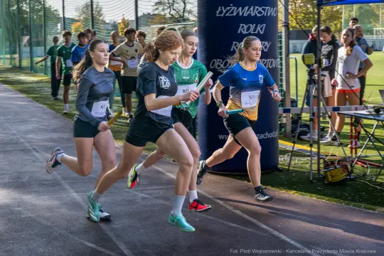Cztery biegaczki startują w sztafecie na boisku sportowym.