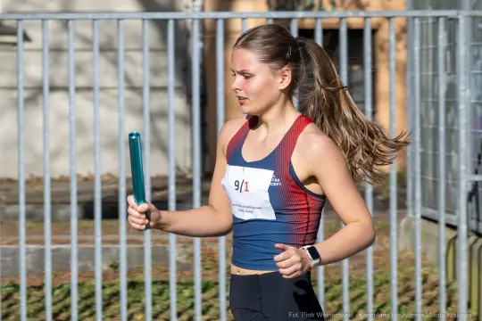 Biegaczka trzymająca pałeczkę sztafetową, w trakcie zawodów lekkoatletycznych.