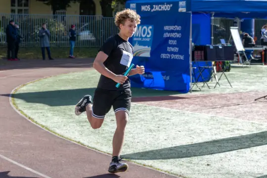 Biegacz na torze lekkoatletycznym z pałeczką w ręku.