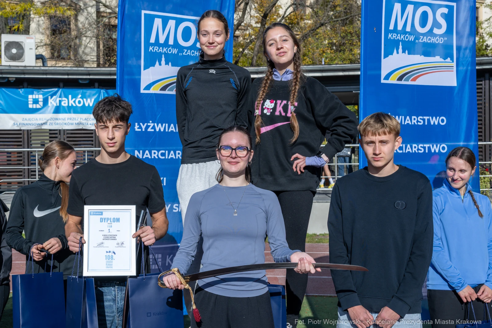 Grupa młodych sportowców z dyplomami i łukiem na tle banerów.  Autor: Piotr Wojnarowski