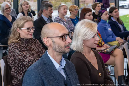 Grupa osób siedzących na wykładzie lub spotkaniu, skupionych na prelegencie.