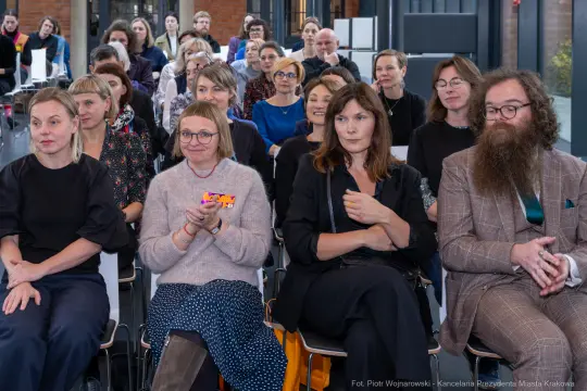 Grupa ludzi siedzących na wydarzeniu, niektórzy klaskają, inni uważnie słuchają.