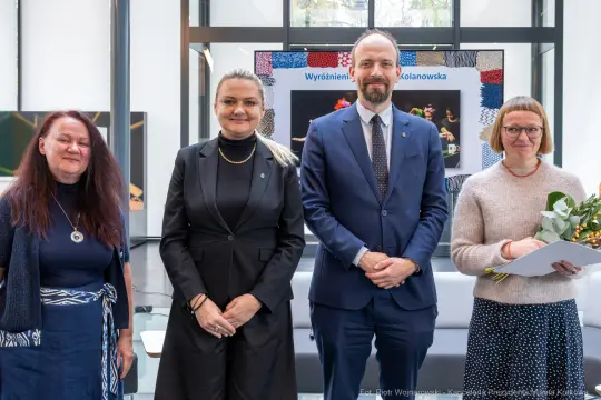 Cztery osoby stojące obok siebie, uśmiechające się, w tle wystawa z nagrodami.