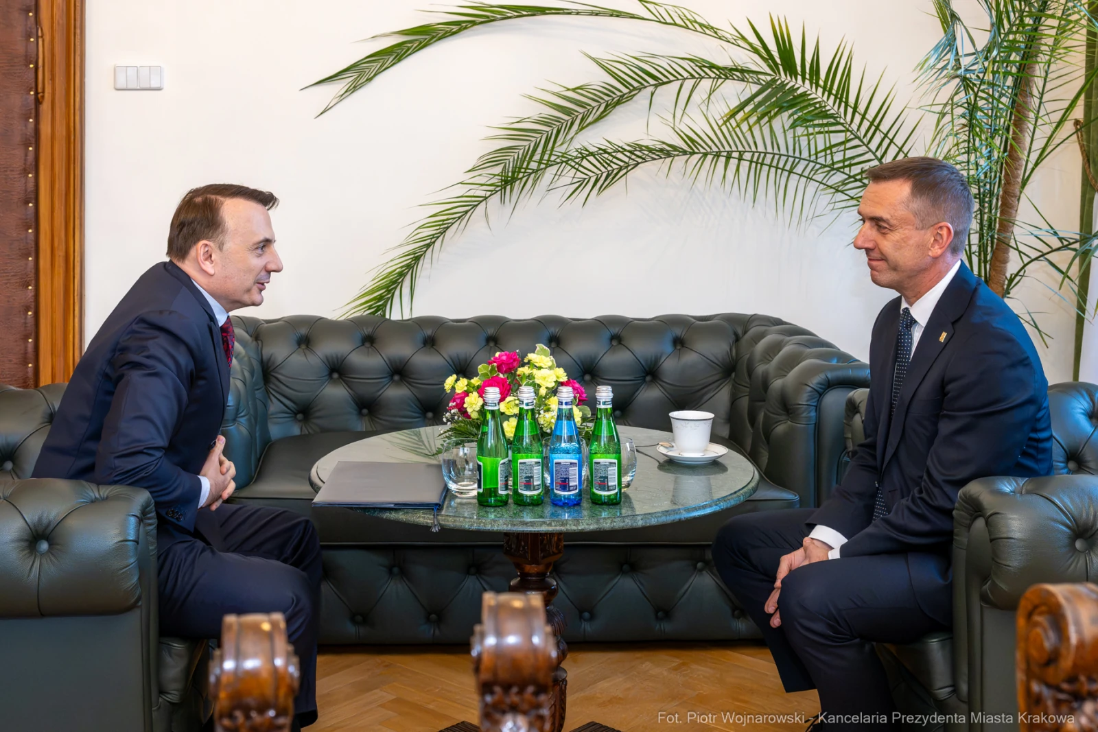 Dwóch mężczyzn rozmawia przy stole z napojami i kwiatami w eleganckim wnętrzu.  Autor: Piotr Wojnarowski