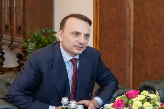 Mężczyzna w garniturze siedzi przy stole z kwiatami i napojami.