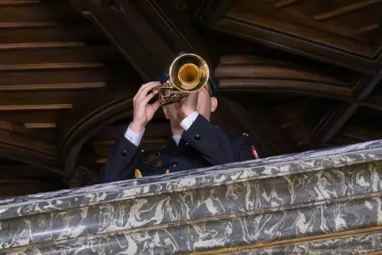 Mężczyzna w mundurze gra na trąbce z balkonu.