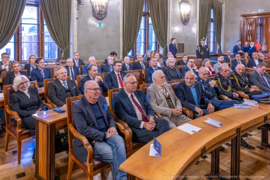 Spotkanie w sali konferencyjnej z udziałem wielu osób w eleganckich strojach.