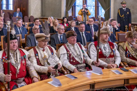 Mężczyźni w tradycyjnych strojach z insygniami, siedzący w sali obrad.