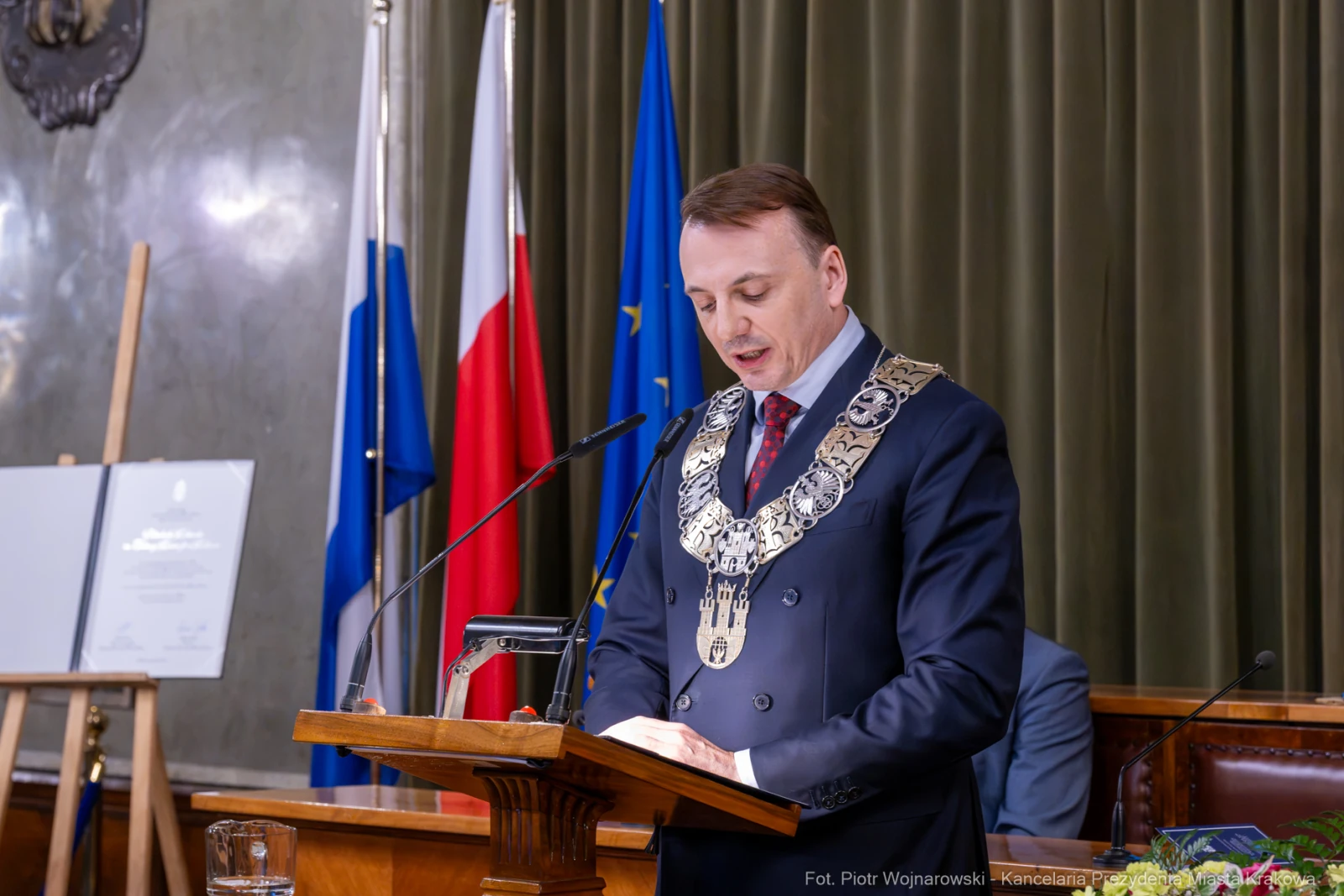 Mężczyzna w łańcuchu prezydenckim przemawia z mównicy w sali obrad. Flagi w tle.  Autor: Piotr Wojnarowski