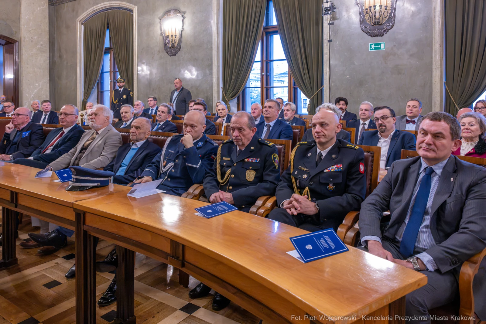Grupa mężczyzn w garniturach i mundurach siedząca w sali podczas uroczystości.  Autor: Piotr Wojnarowski