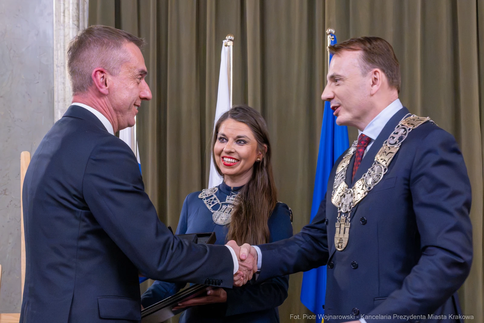 Ceremonia wręczenia nagrody z uściskiem dłoni między mężczyznami i uśmiechającą się kobietą w tle.  Autor: Piotr Wojnarowski