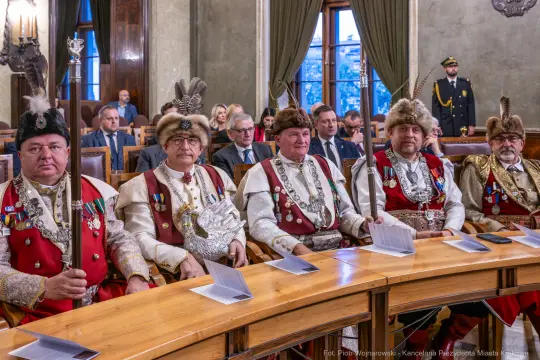 Grupa mężczyzn w tradycyjnych strojach, siedzących przy stole w sali obrad.