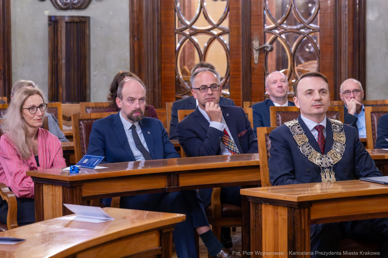 Grupa osób siedzących przy stole w sali konferencyjnej, w tym mężczyzna w łańcuchu prezydenckim.  Autor: Piotr Wojnarowski