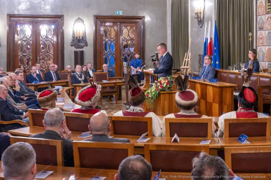 Uroczystość w sali obrad z mówcą i uczestnikami w tradycyjnych strojach.