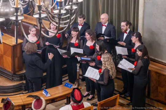 Chór wykonujący utwór muzyczny w eleganckich strojach, z nutami w rękach.