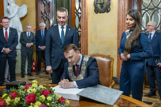 Prezydent podpisuje dokument w otoczeniu urzędników i gości.