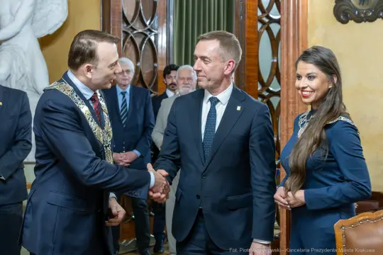 Uroczystość wręczenia odznaczeń w eleganckim wnętrzu z gośćmi.