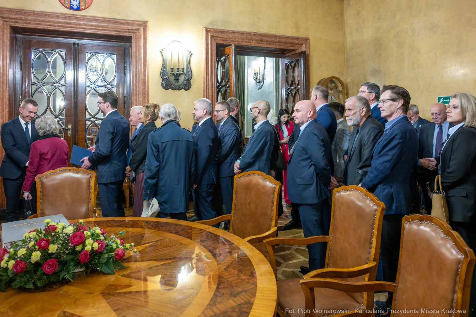 Grupa ludzi w formalnych strojach w sali z dużym stołem i dekoracjami.  Autor: Piotr Wojnarowski