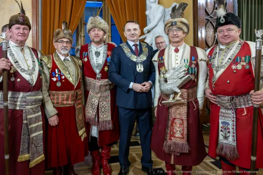 Grupa mężczyzn w tradycyjnych strojach z medalami, pozująca do zdjęcia w eleganckim wnętrzu.