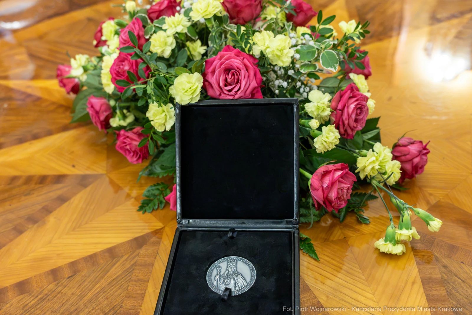 Medal w czarnej etui obok bukietu róż i innych kwiatów.  Autor: Piotr Wojnarowski