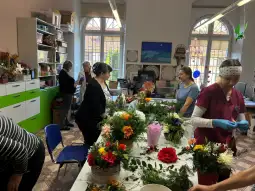 Warsztat florystyczny z kobietami tworzącymi bukiety i kompozycje kwiatowe.