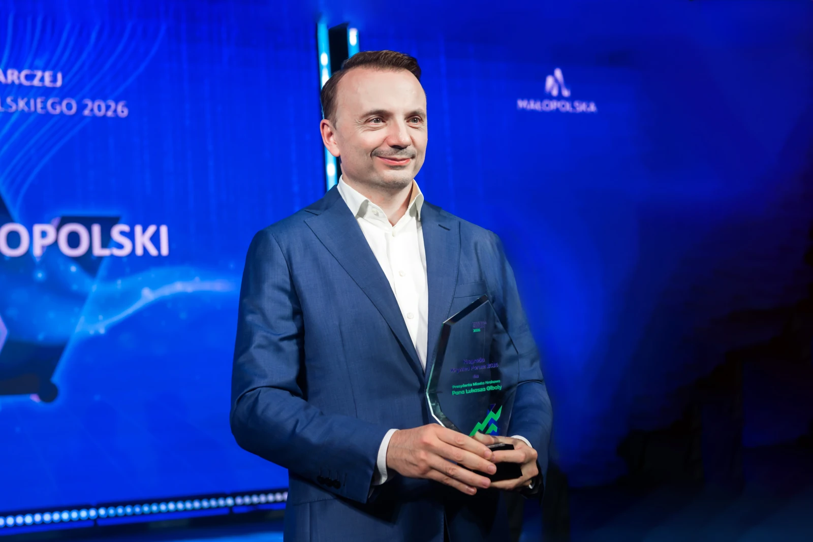 Mężczyzna w garniturze trzyma statuetkę na tle niebieskiego tła.  Autor: Urząd Marszałkowski Województwa Małopolskiego