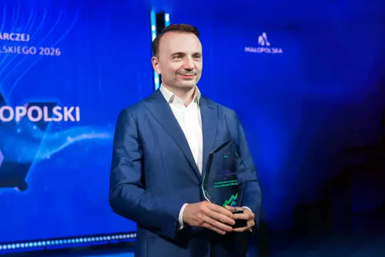 Mężczyzna w garniturze trzyma statuetkę na tle niebieskiego tła.