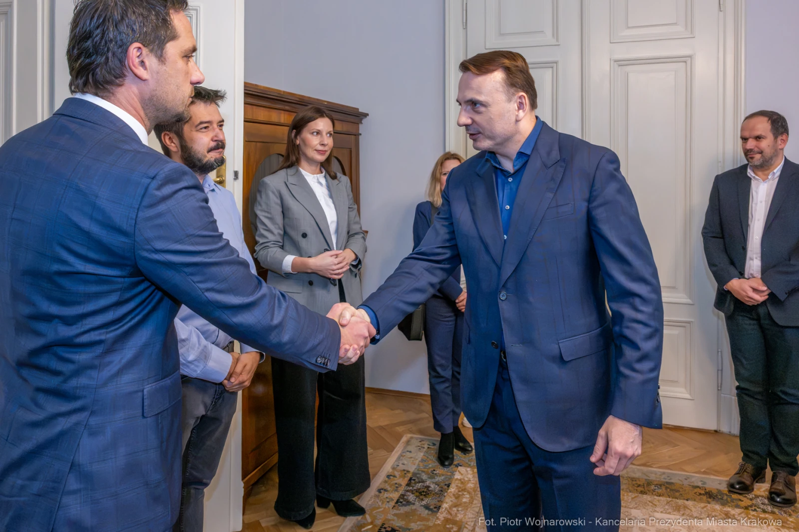 Spotkanie dwóch mężczyzn przy uścisku dłoni, w tle grupa osób.  Autor: Piotr Wojnarowski