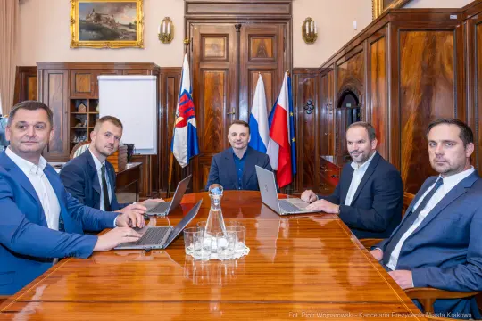 Pięciu mężczyzn w garniturach siedzących przy stole w sali konferencyjnej.