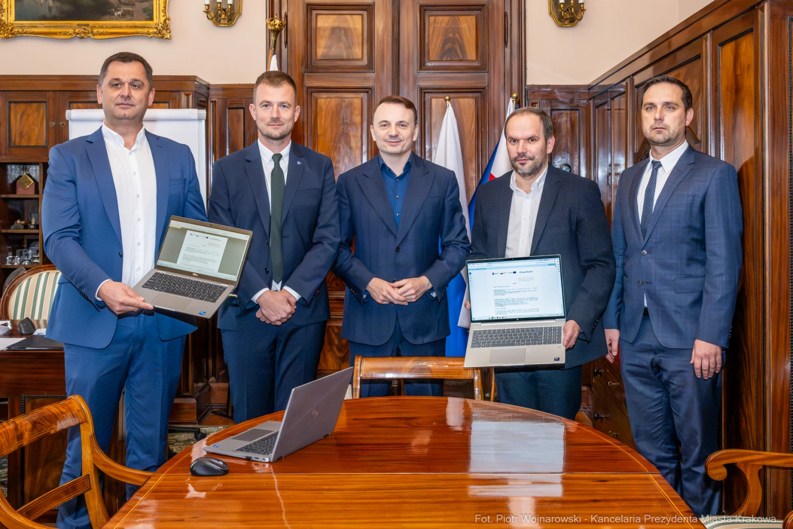 Pięciu mężczyzn w garniturach prezentuje laptopy w biurze.  Autor: Piotr Wojnarowski