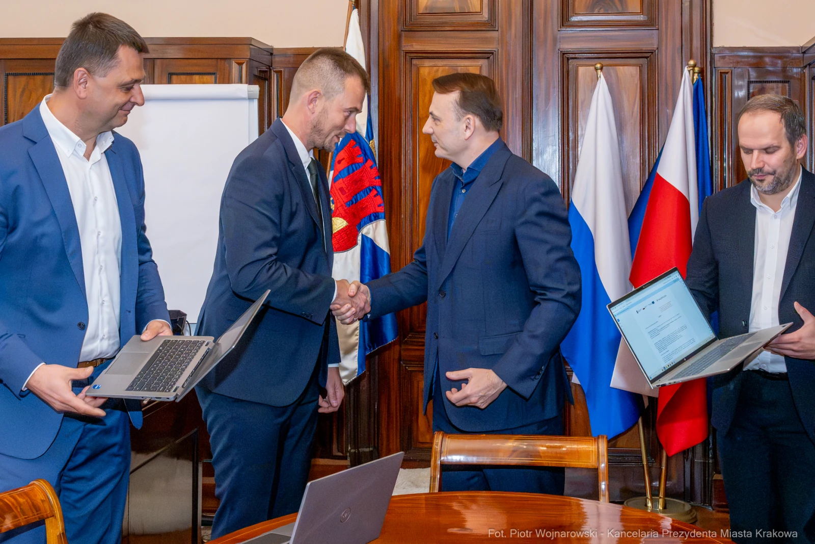 Spotkanie przedstawicieli władz z laptopami, uścisk dłoni. Flagi w tle.  Autor: Piotr Wojnarowski