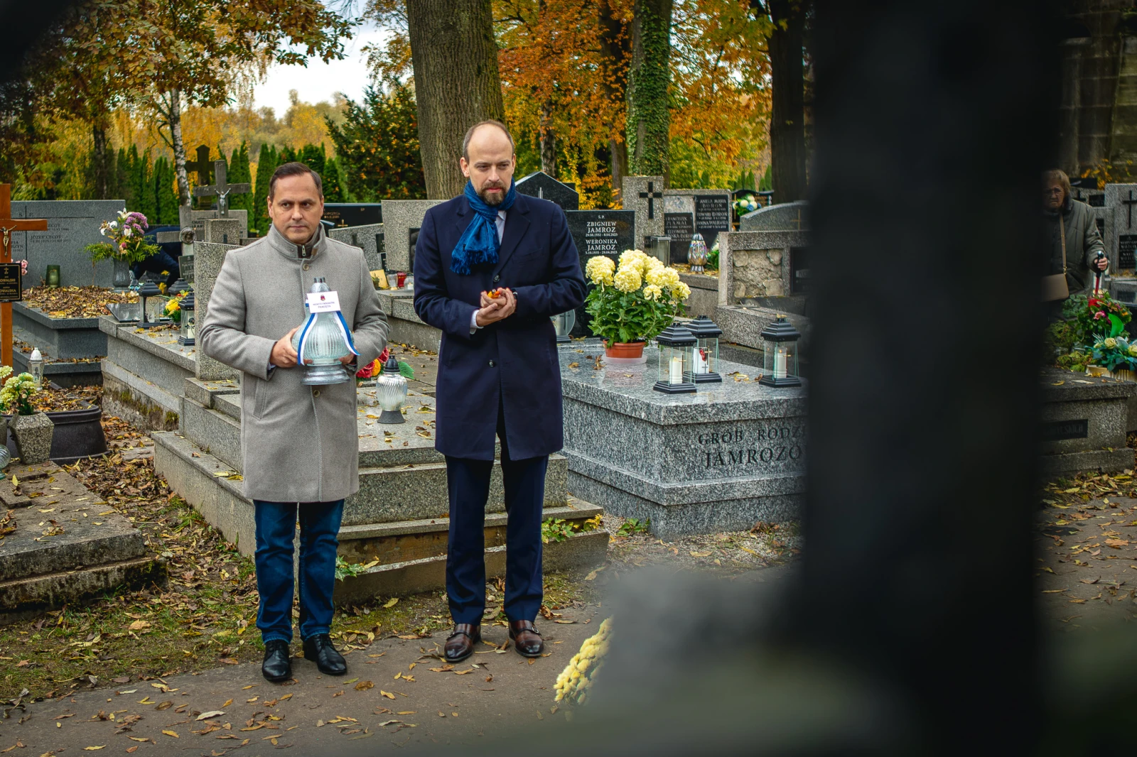 Dwaj mężczyźni na cmentarzu, trzymają lampion i modlą się przy grobie. Jesienna sceneria.  Autor: Tom Rollauer