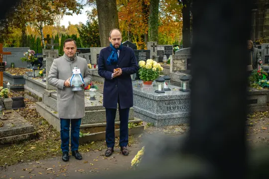 Dwaj mężczyźni na cmentarzu, trzymają lampion i modlą się przy grobie. Jesienna sceneria.