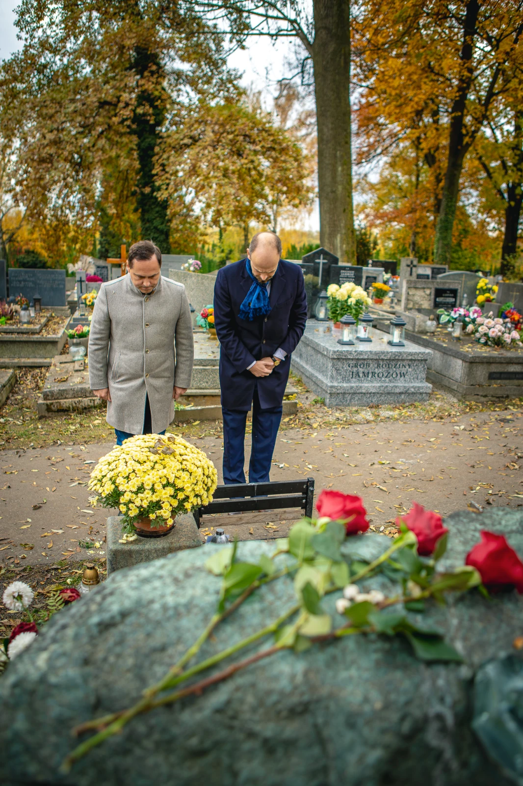 Dwóch mężczyzn składa hołd na cmentarzu, obok kwiaty i znicze.  Autor: Tom Rollauer