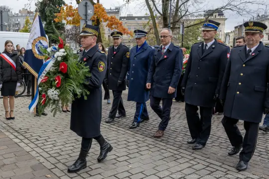 Uroczystość złożenia wieńca przez delegację w mundurach, z flagami i kwiatami.