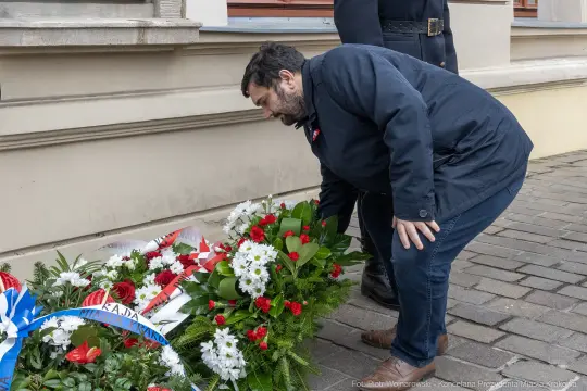 Mężczyzna składa kwiaty przy pomniku, otoczony zielenią i dekoracjami.