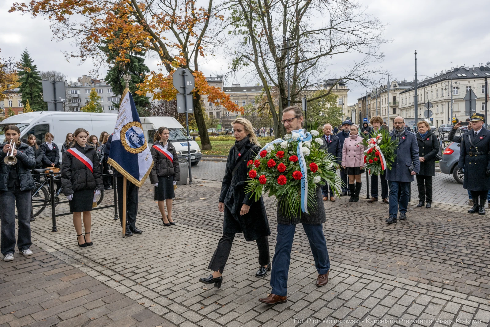 Uroczystość złożenia wieńca, uczestnicy w strojach formalnych, flagi i muzyka.  Autor: Piotr Wojnarowski