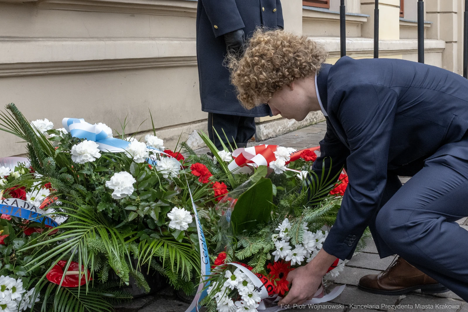 Młody mężczyzna składa kwiaty w hołdzie, obok widoczne inne wieńce.  Autor: Piotr Wojnarowski