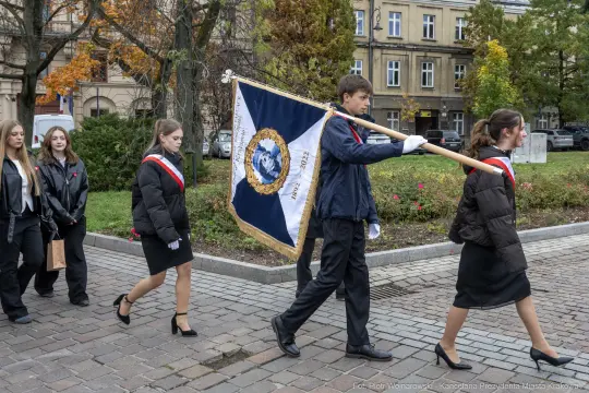 Młodzież niosąca sztandar podczas uroczystości na ulicy.