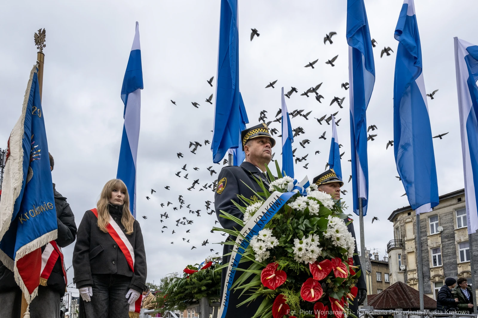 Uroczystość z flagami, wieńcami i uczestnikami, w tle ptaki w locie.  Autor: Piotr Wojnarowski