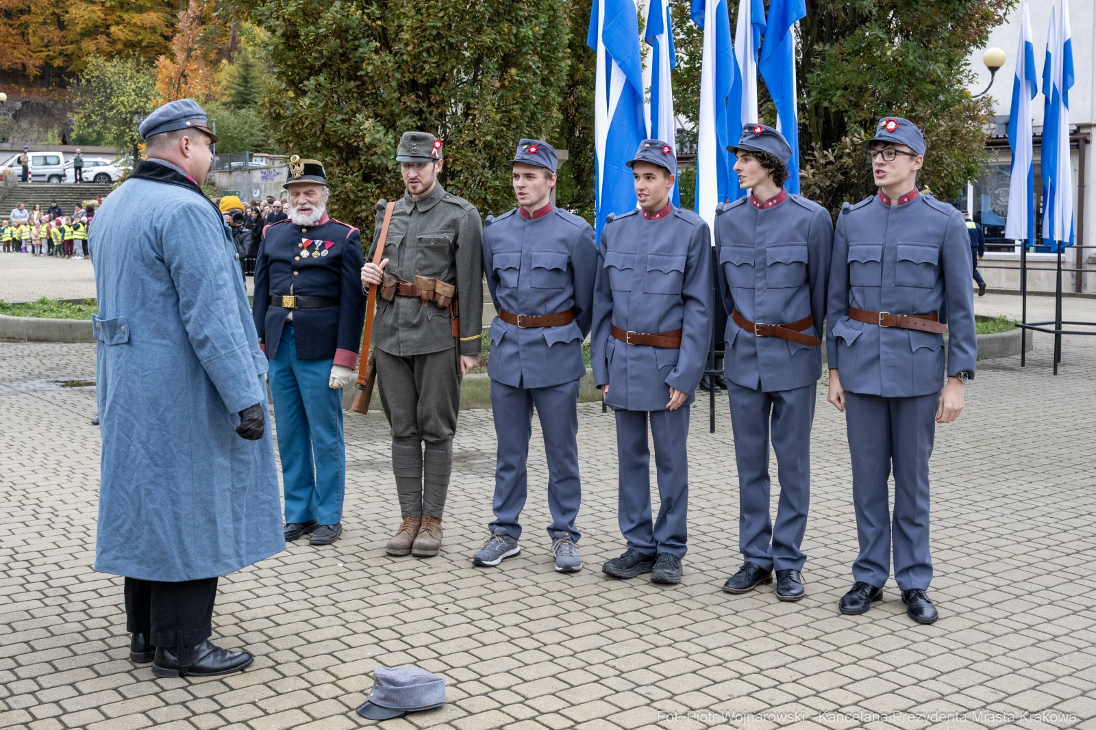 Grupa mężczyzn w mundurach wojskowych podczas ceremonii, z flagami w tle.  Autor: Piotr Wojnarowski