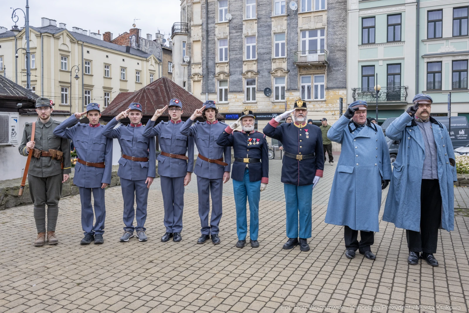 Grupa mężczyzn w mundurach wojskowych, salutujących na tle budynków.  Autor: Piotr Wojnarowski