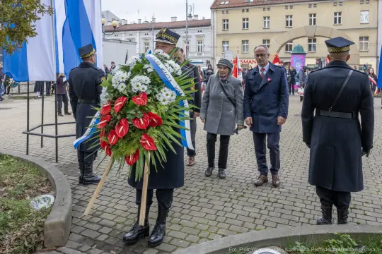 Uroczystość złożenia wieńca w towarzystwie osób w mundurach i flag.