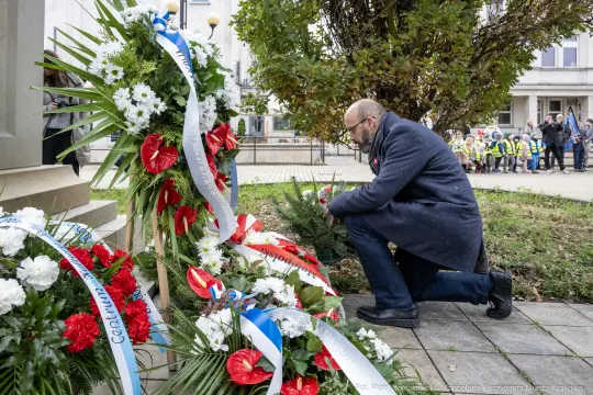 Mężczyzna klęczy przy kwiatach i zniczach, składając hołd.