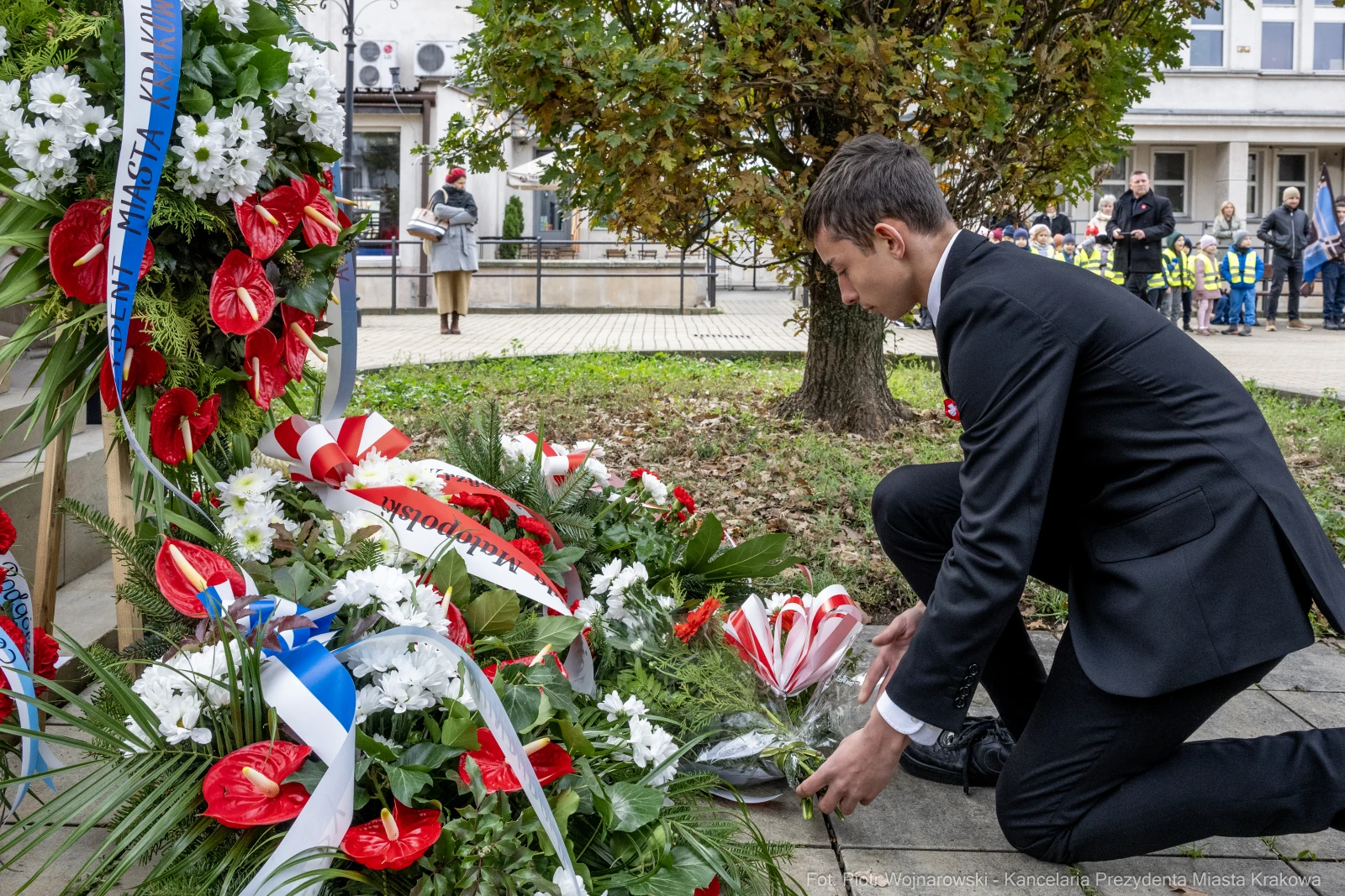 Mężczyzna składa kwiaty przy pomniku, w tle dzieci w strojach szkolnych.  Autor: Piotr Wojnarowski