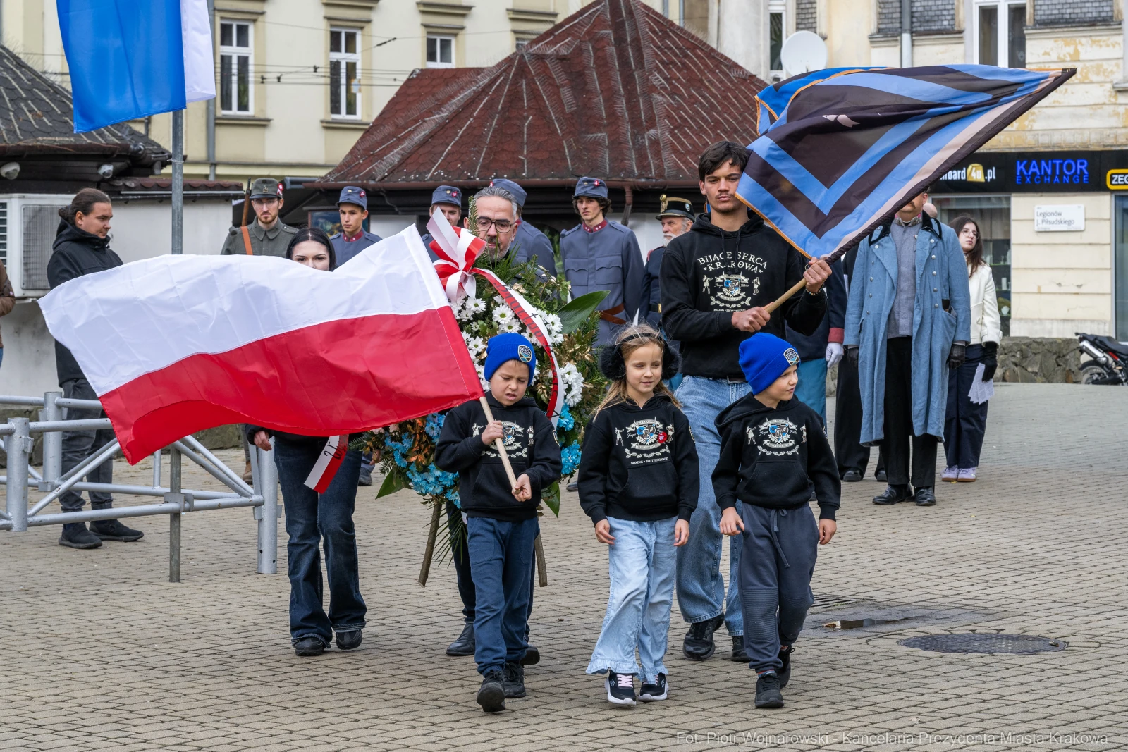 Uczestnicy ceremonii z flagami i kwiatami, dzieci w bluzach z logo.  Autor: Piotr Wojnarowski
