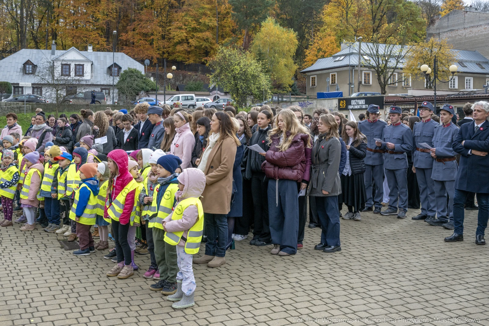 Grupa dzieci w kamizelkach odblaskowych oraz dorosłych podczas uroczystości na świeżym powietrzu.  Autor: Piotr Wojnarowski