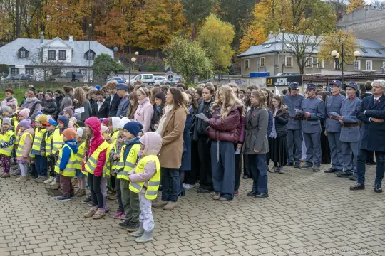 Grupa dzieci w kamizelkach odblaskowych oraz dorosłych podczas uroczystości na świeżym powietrzu.