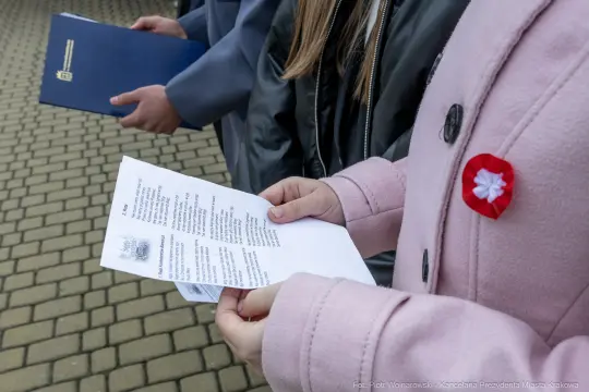 Osoby trzymające dokumenty i kartki, jedna z nich z przypinką w kształcie flagi.